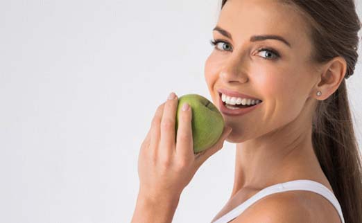 smiling woman biting into a green apple