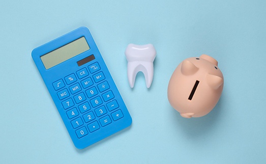 A calculator, model tooth, and piggy bank set against a blue background